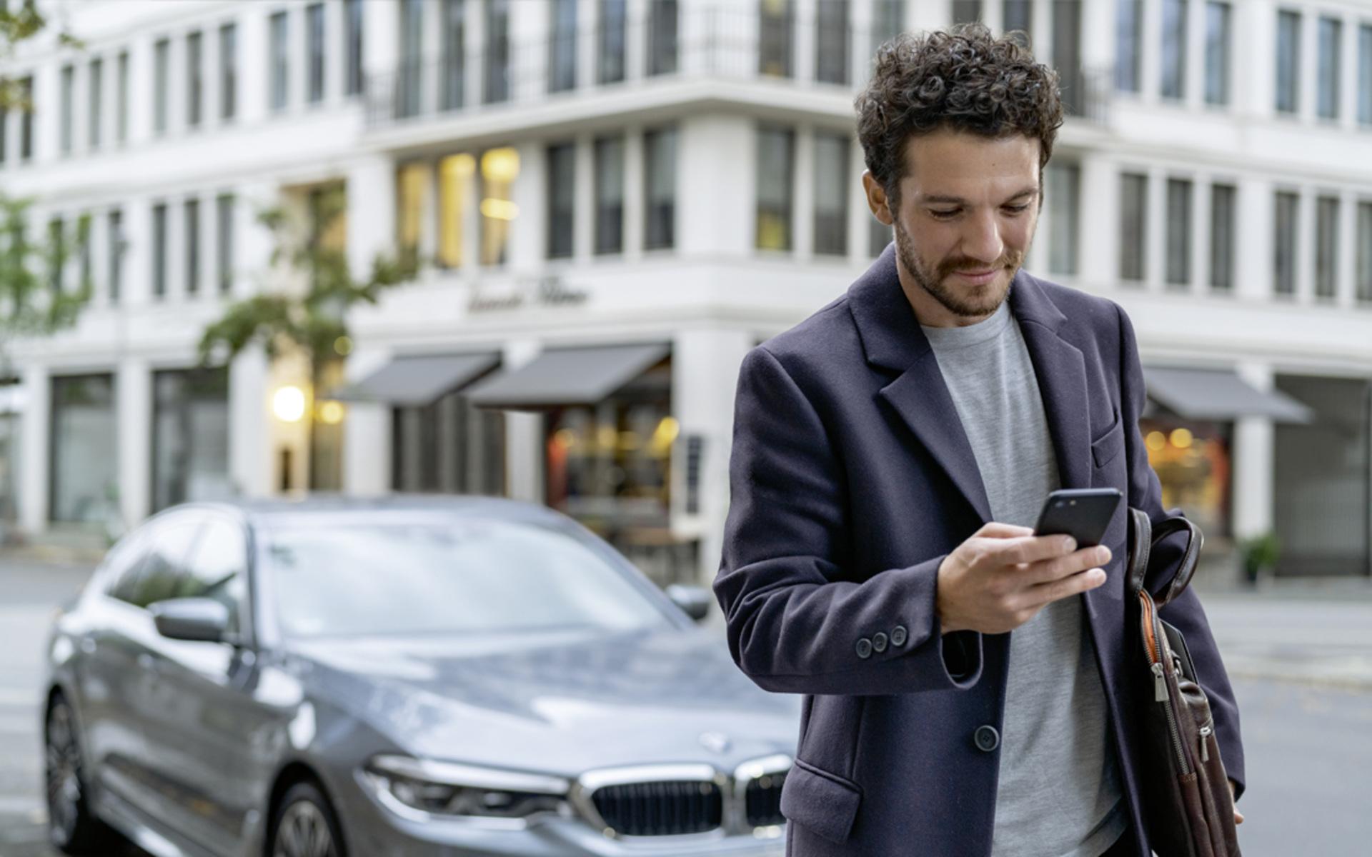 Mann schaut auf Smartphone vor BMW