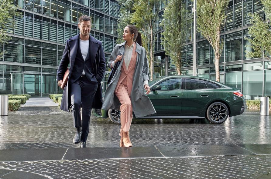 Mann und Frau in Business Look laufen Treppe hoch, im Hintergrund dunkelgrüner Wagen
