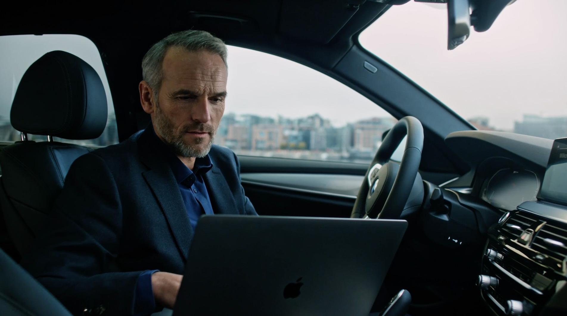 Mann sitzt im Auto mit Laptop