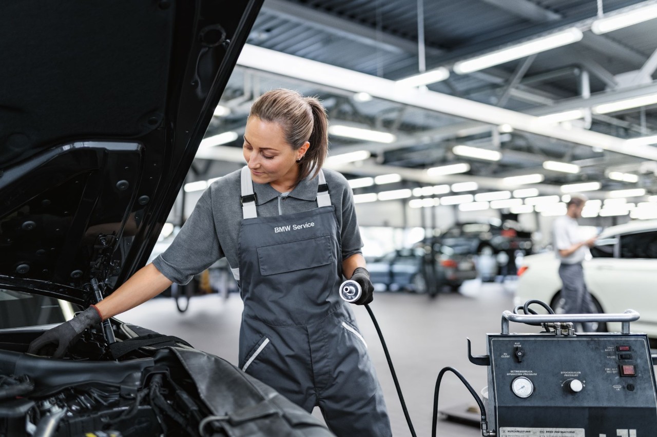 Frau steht neben einer offenen Motorhaube und fuellt die Bremsfluessigkeit nach
