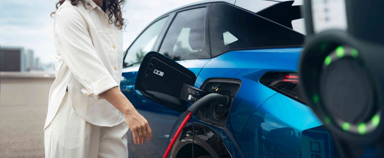 Frau laedt Elektroauto an Ladestation auf.