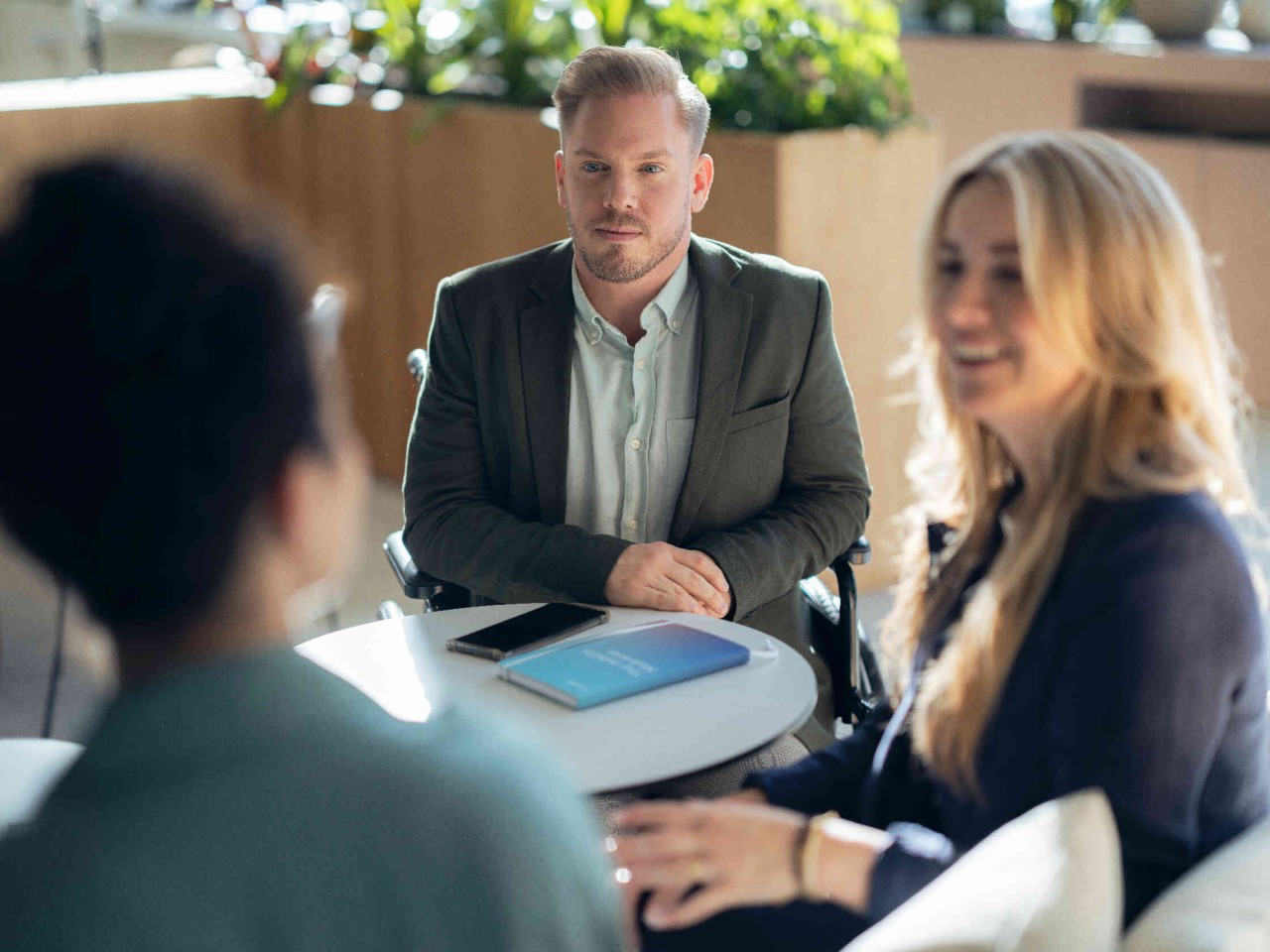 Drei Personen an rundem Tisch im hellen Raum.