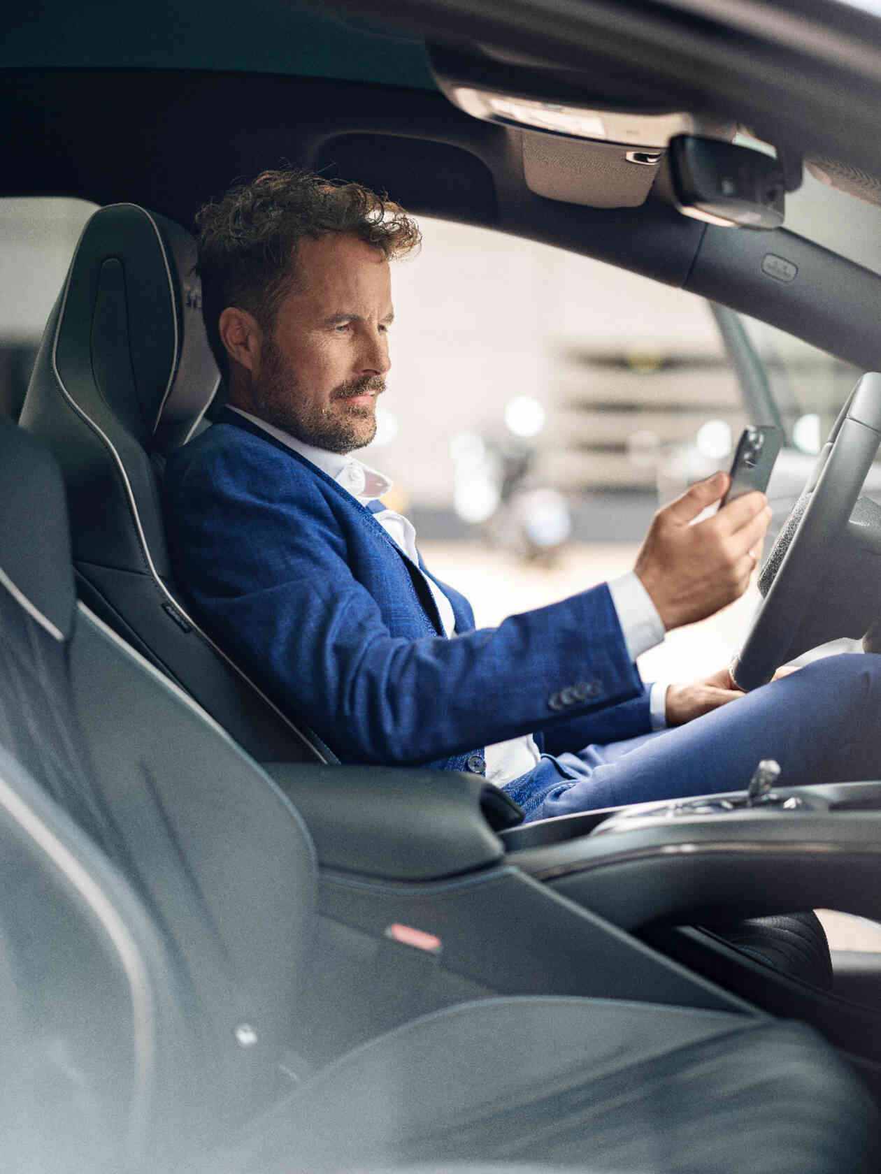 Mann sitzt auf dem Fahrersitz im Auto und schaut auf sein Handy Fahrertuer Perspektive.