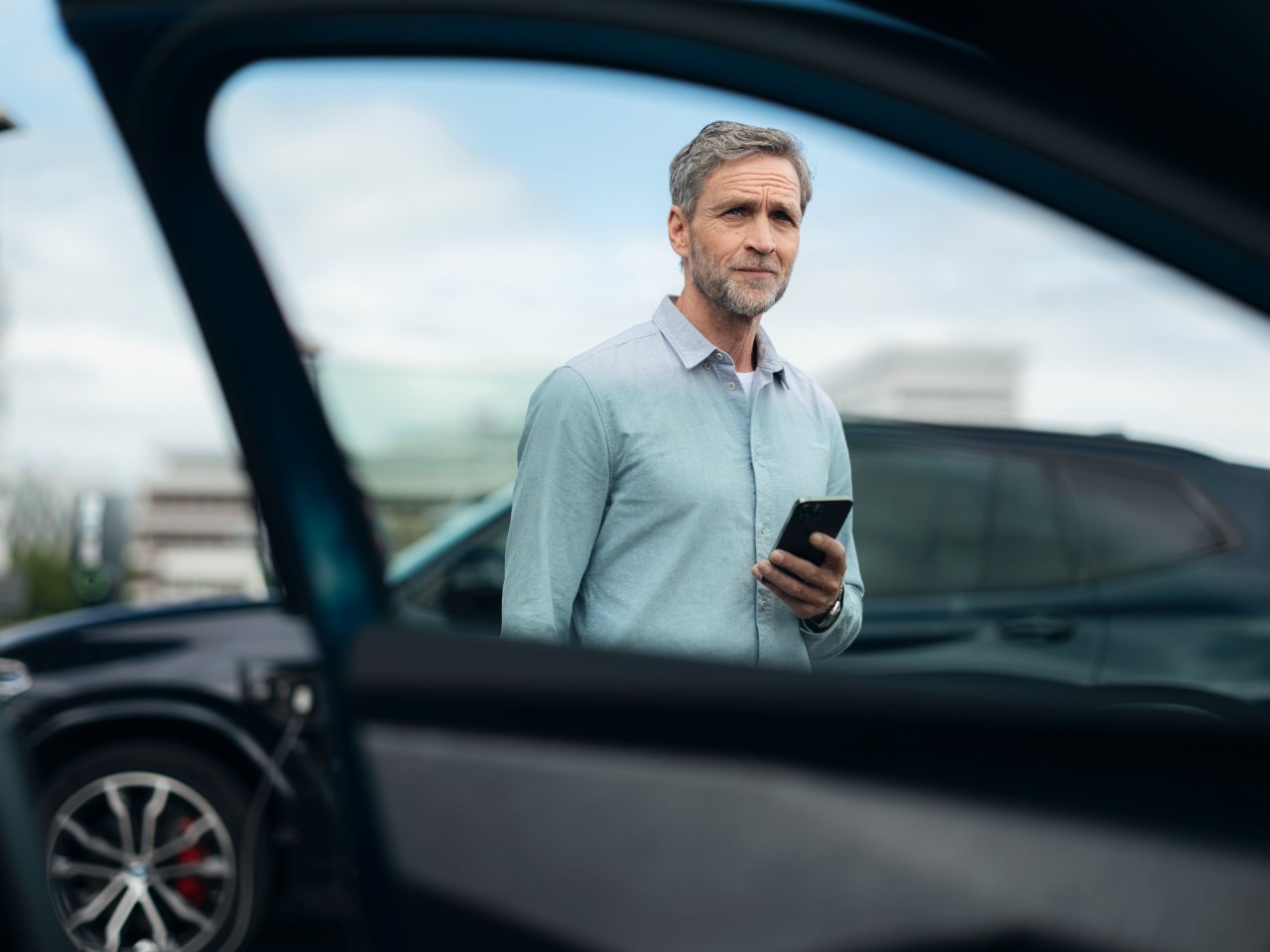 Ein Mann steht auf einem Parkplatz mit einem Smartphone in der Hand.