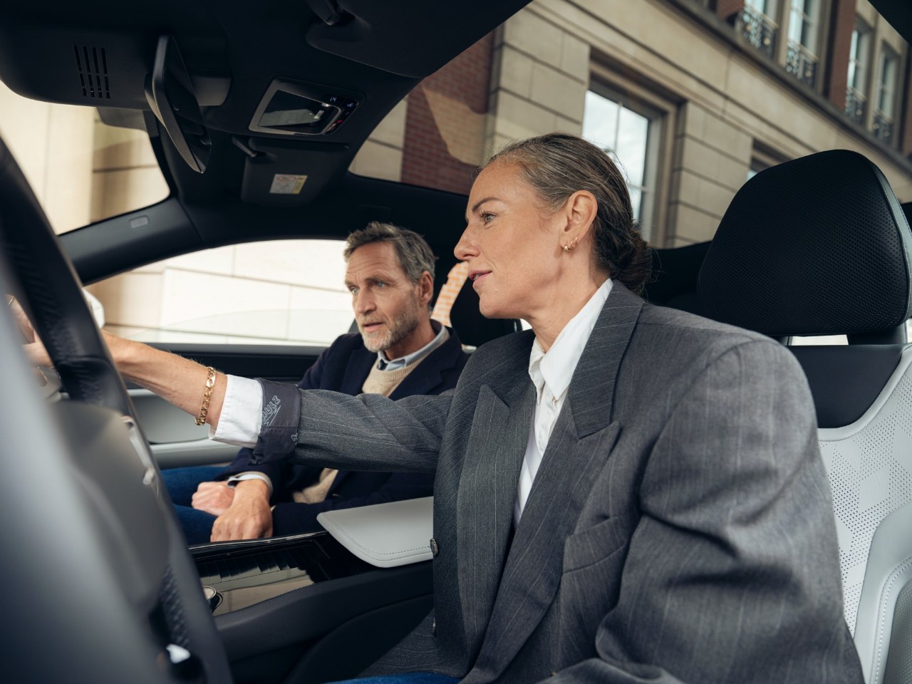 Zwei Personen in Blazern sitzen in einem Auto und schauen auf das zentrale Display.