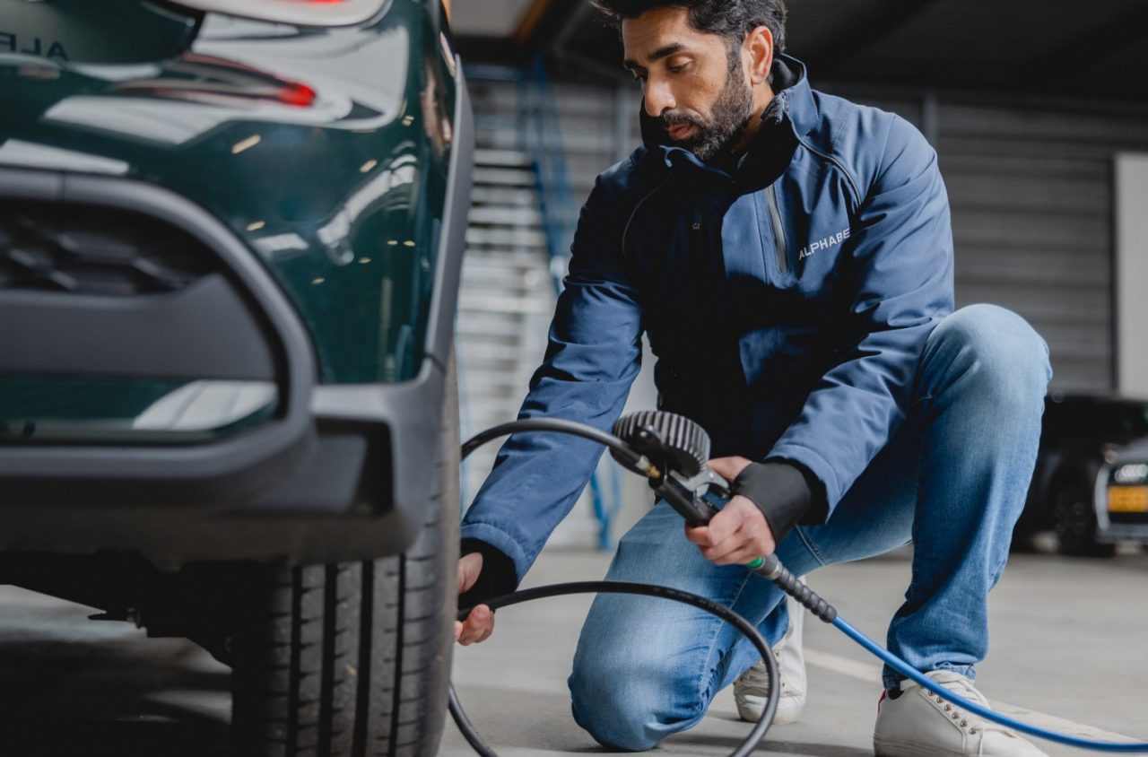 Eine Person in einer Alphabet-Jacke überprüft und pumpt den Reifen eines Autos in einer gut beleuchteten Tiefgarage auf.