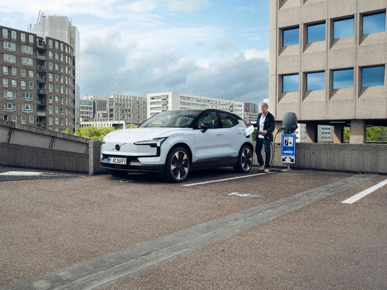 Mann laedt Elektroauto auf staedtischem Parkdeck mit modernen Gebaeuden.