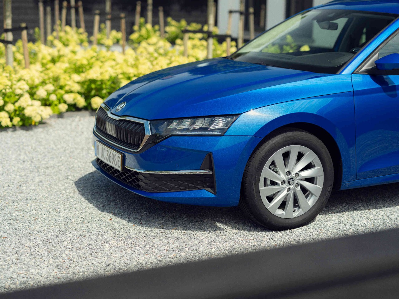 Front eines blauen Skoda auf Kiesweg markanter Kuehlergrill und Scheinwerfer sichtbar.