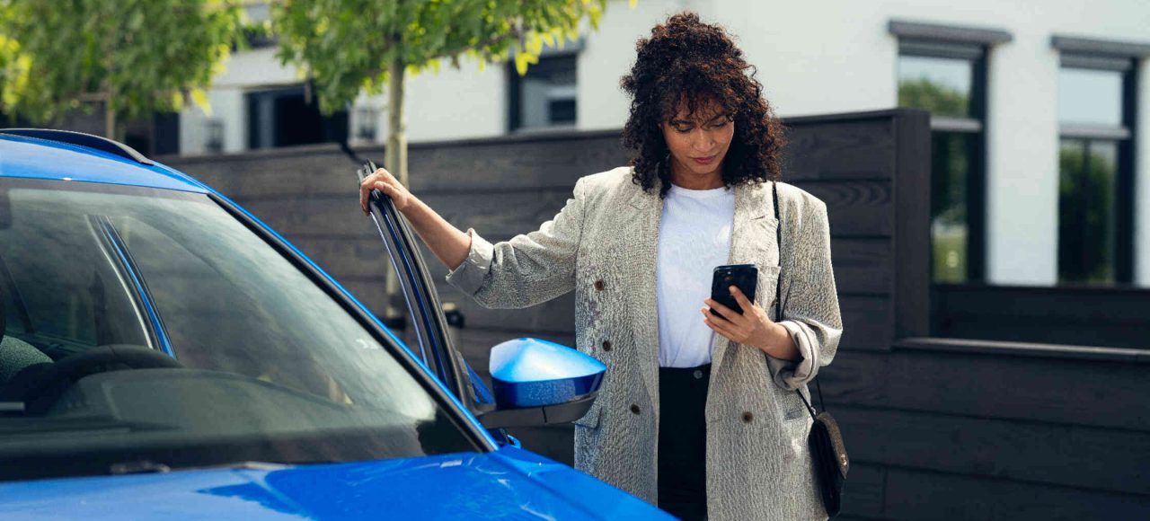 Frau neben blauem Auto haelt Fahrertuer offen.