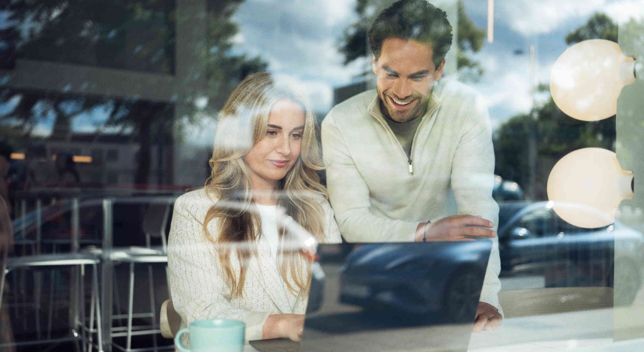 Zwei Personen in einem Cafe arbeiten an einem Laptop.