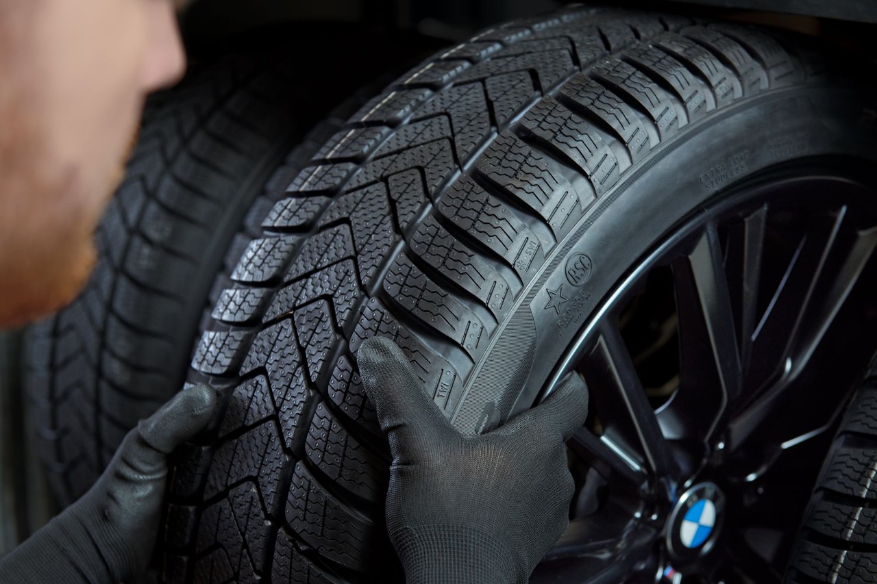 Nahaufnahme eines Mannes mit schwarzen Arbeitshandschuhen der einen Autoreifen ueberprueft