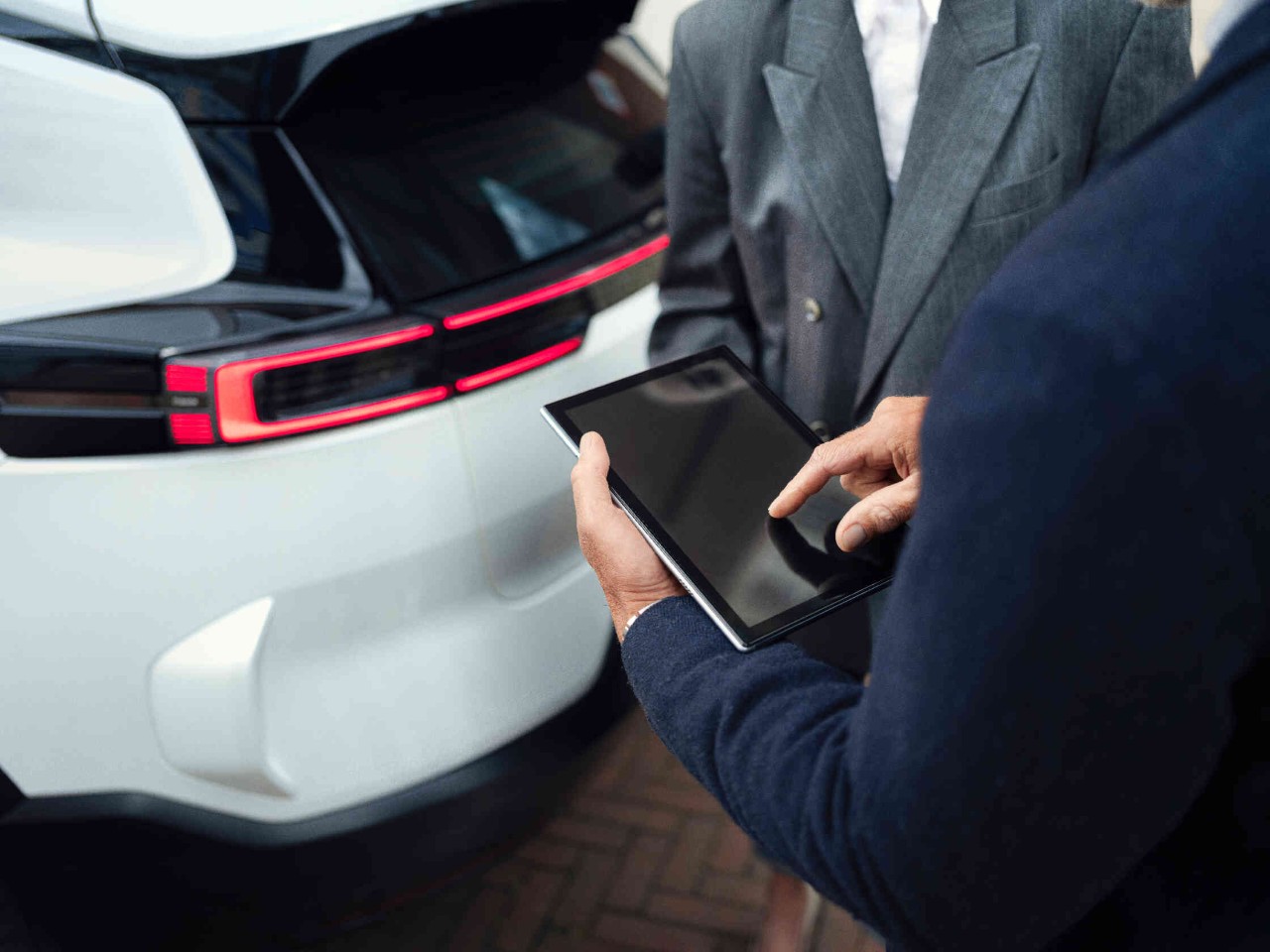 Person haelt Tablet und steht neben weiterer Person in grauem Anzug.