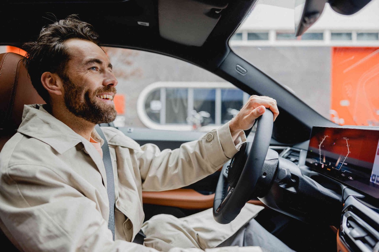 Mann sitzt am Steuer eines modernen PKW und blickt laechelnd nach vorne