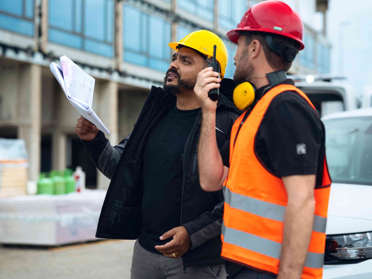 Zwei Personen mit Schutzhelmen kommunizieren auf Baustelle.