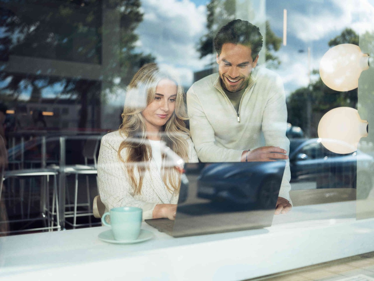 Zwei Personen in einem Cafe arbeiten an einem Laptop.