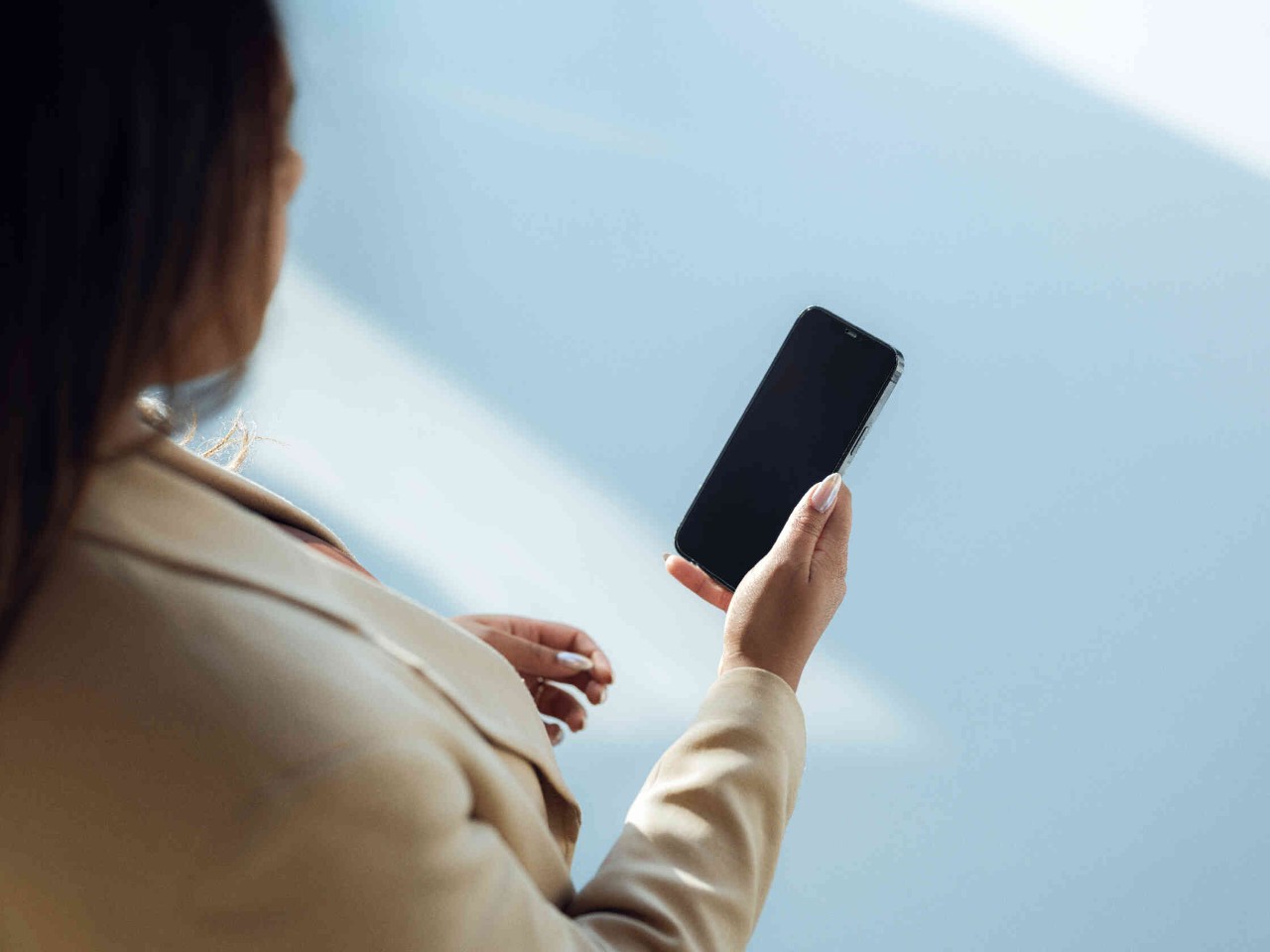 Frau haelt Smartphone in einem hellen Raum mit sanftem Hintergrund.