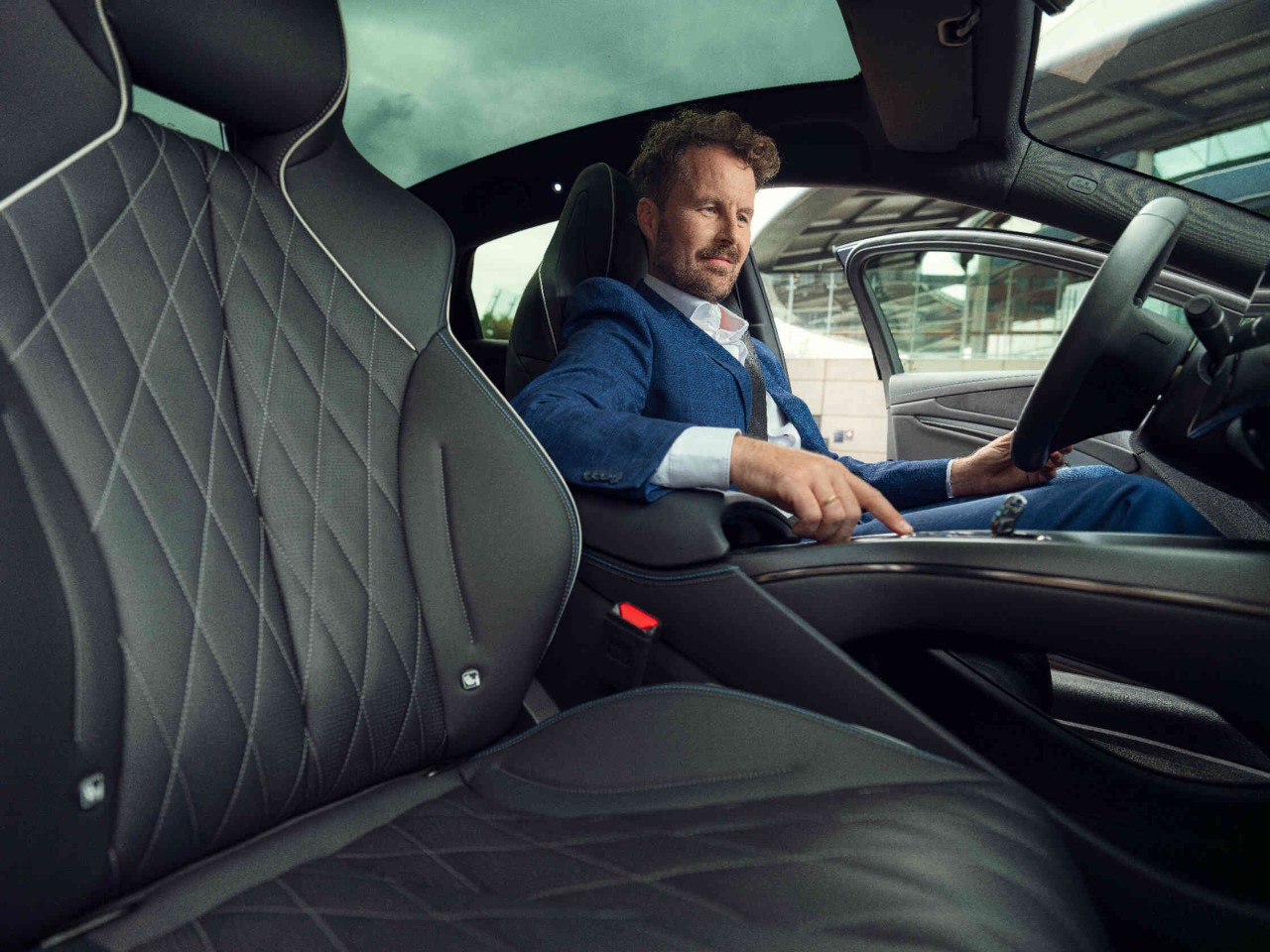 Fahrer bedient die Mittelkonsole in stehendem Auto bei offener Tuere.