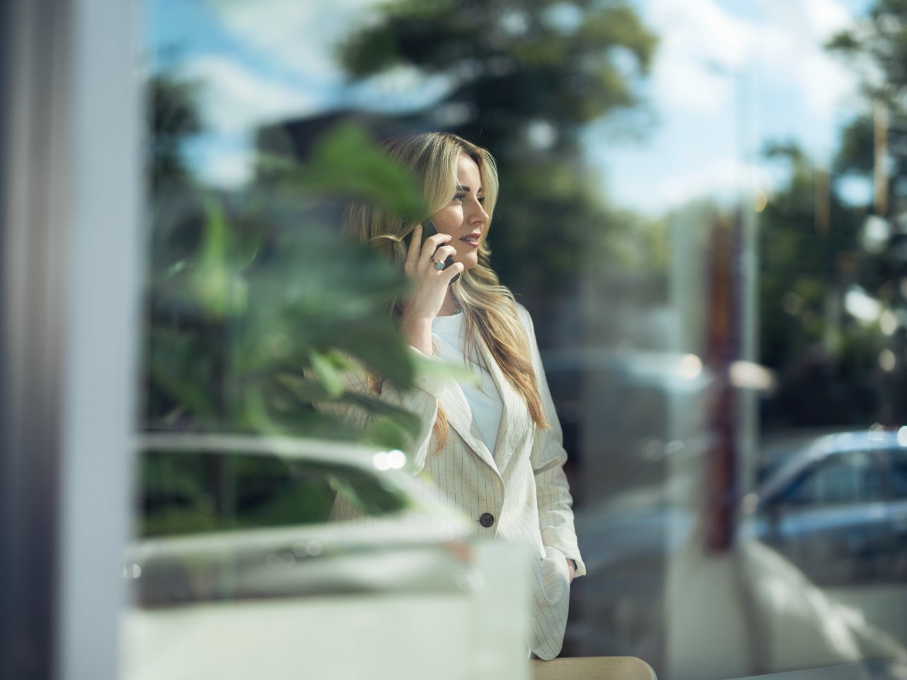 Frau am Telefon mit blonden Harren schaut aus dem Fenster