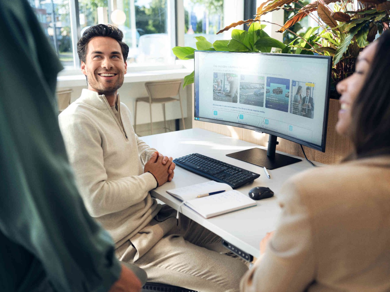 Personen sitzen laechelnd vor grossem Computer Bildschirm.