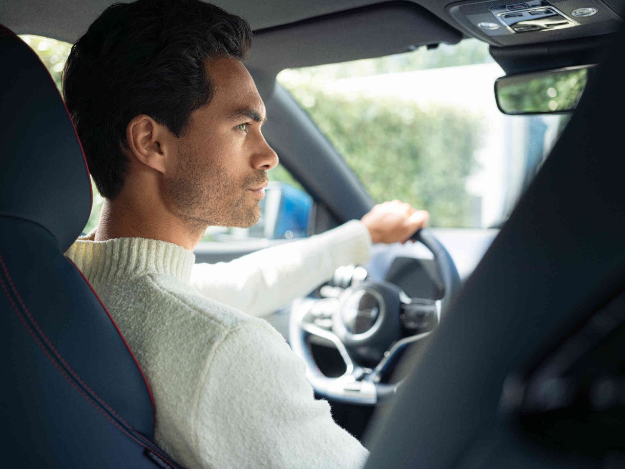 Mann im Auto mit cremefarbenem Pullover stilvoller Innenraum mit roten Naehten.