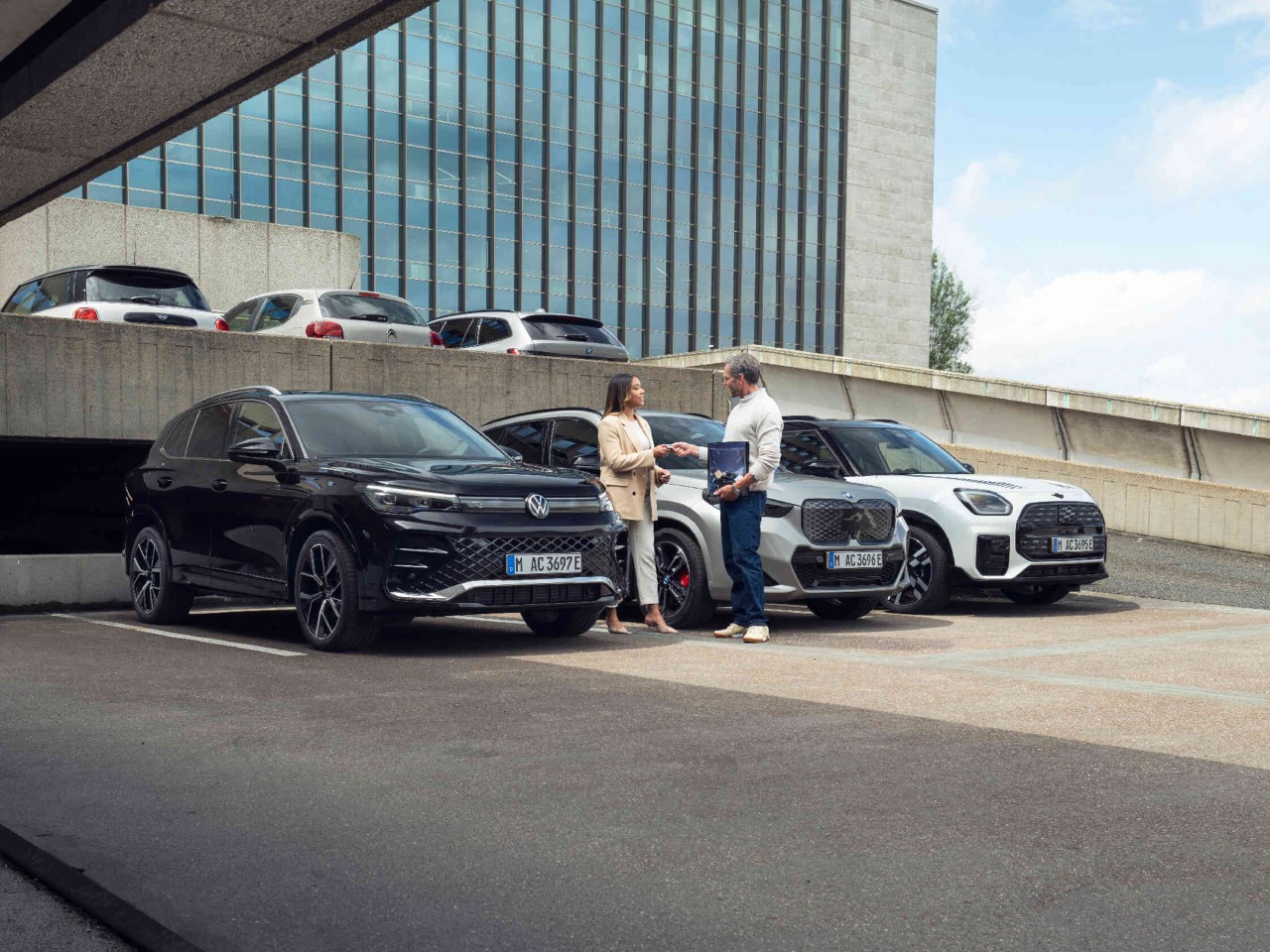 Zwei Personen interagieren zwischen geparkten Autos auf urbanem Parkplatz.