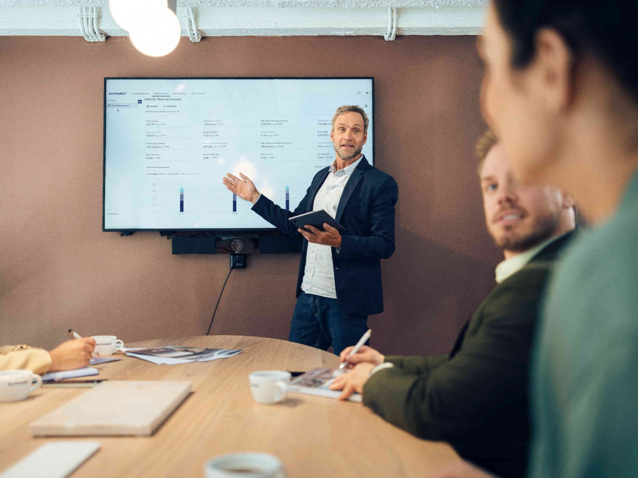 Mann haelt Praesentation ueber Fahrzeugflottenemissionen vor grossem Bildschirm im Konferenzraum.