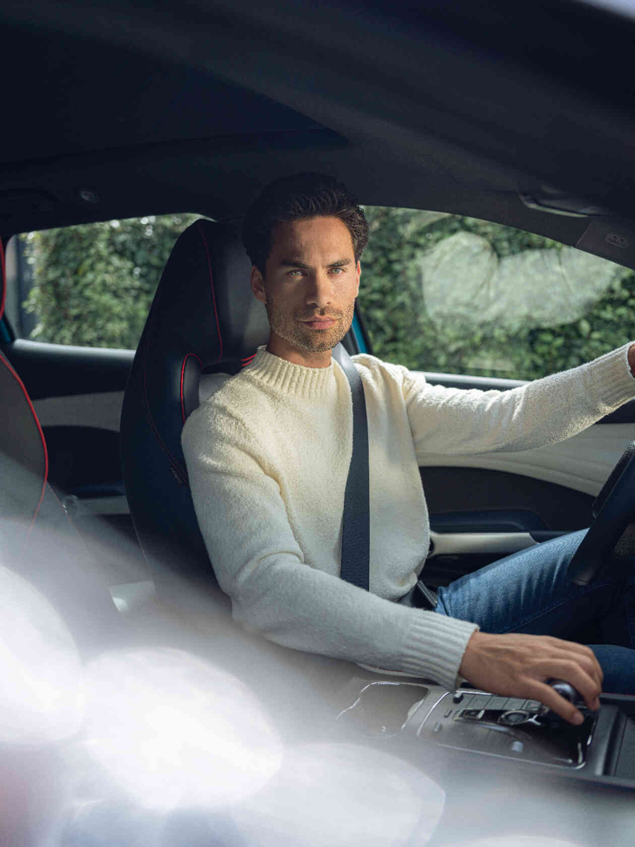 Mann im Auto mit cremefarbenem Pullover bedient Mittelkonsole.