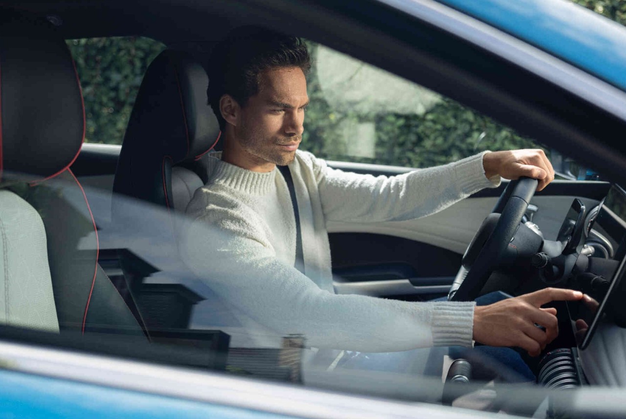 Mann im modernen Auto bedient Touchscreen traegt cremefarbenen Pullover stilvoller Innenraum.