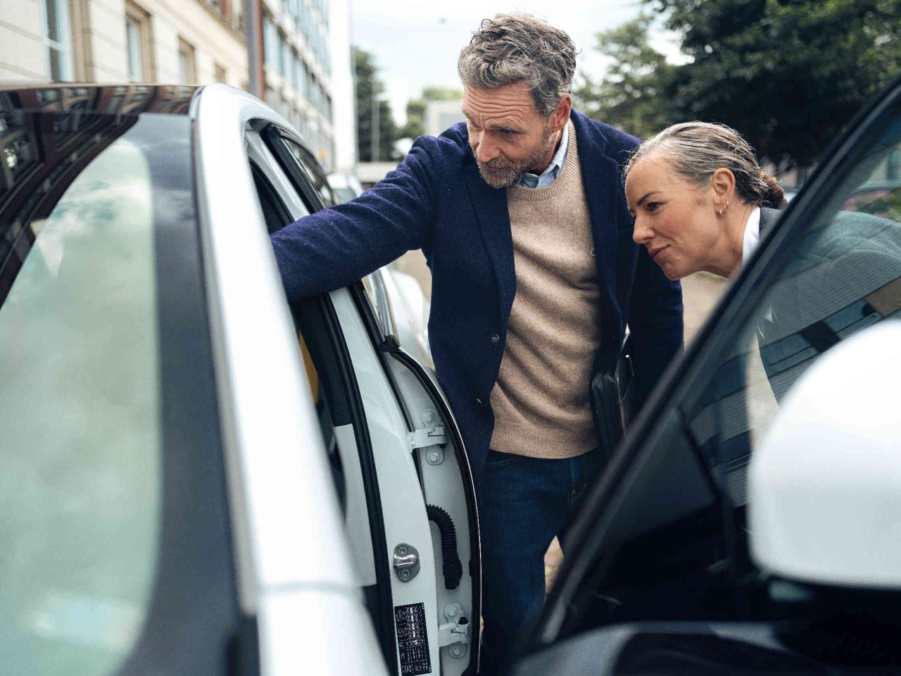 Mann und Frau stehen neben weissem Auto und schauen bei offener Fahrertuer hinein.