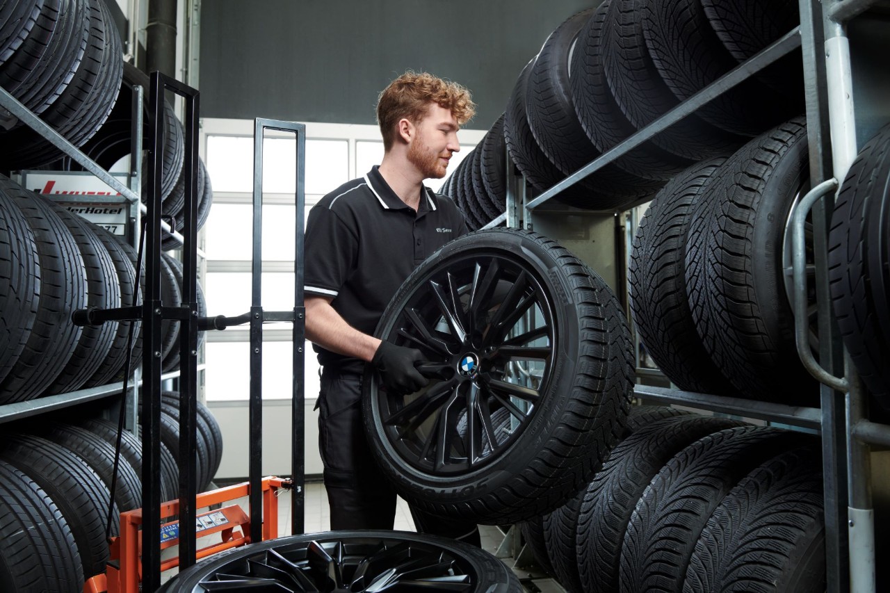 Mann steht im Reifenlager und haelt einen Reifen 