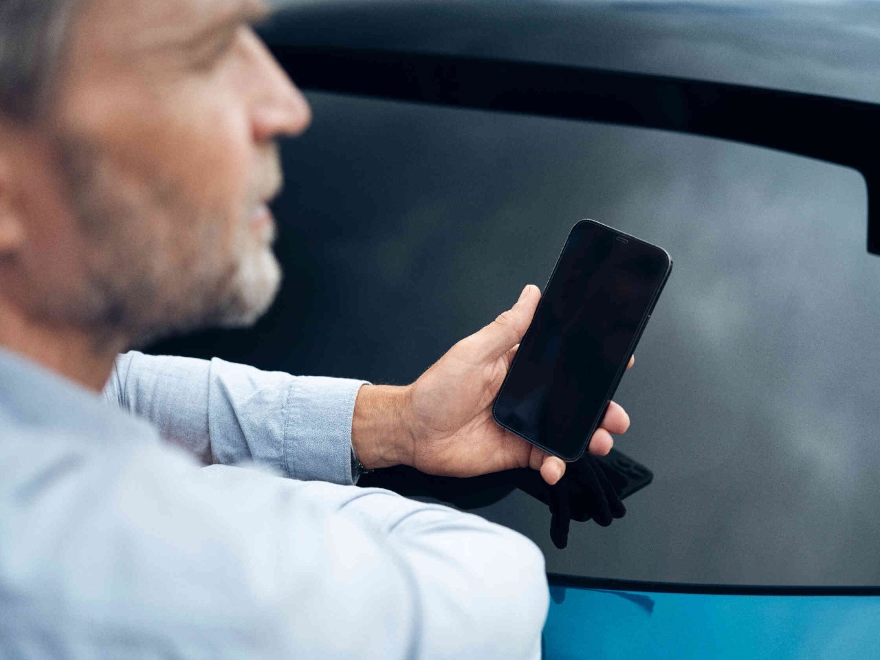 Mann in hellblauem Hemd haelt Smartphone.