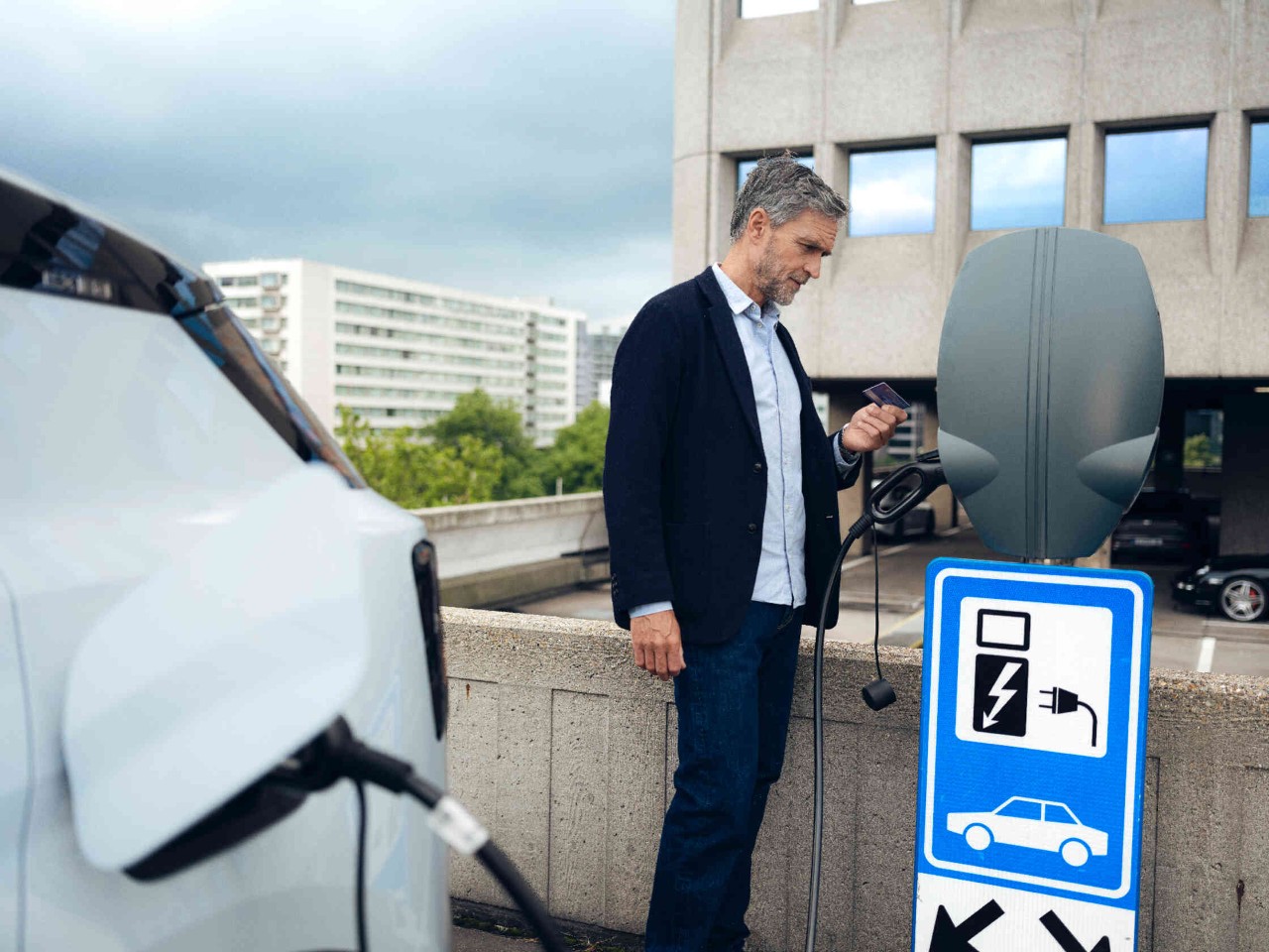 Ein Mann steht neben einer Ladestation fuer Elektrofahrzeuge auf einem Parkdeck haelt eine Karte in der Hand.