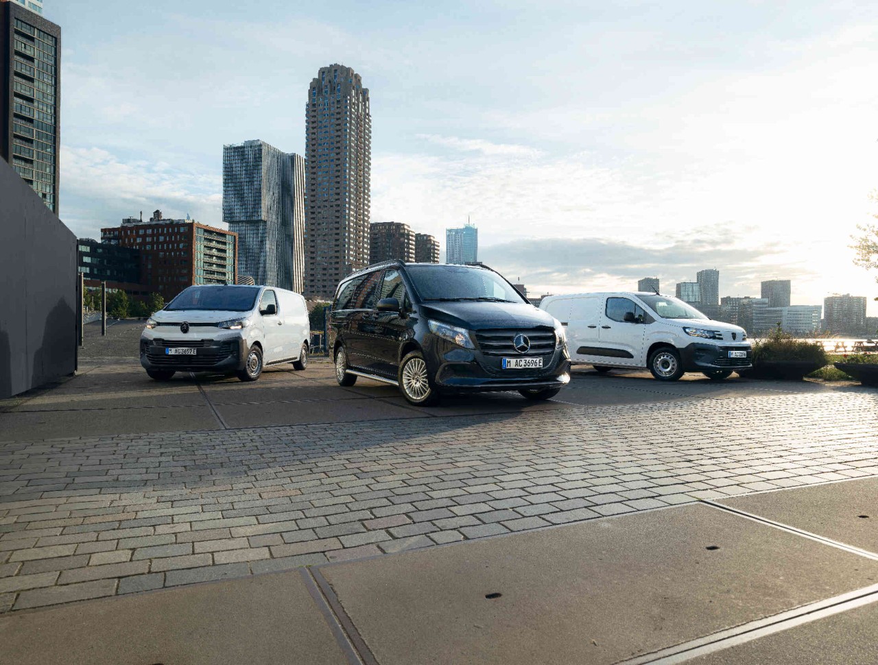 Drei Transporter stehen auf Pflastersteinen Hintergrund zeigt Hochhaeuser und Sonnenuntergang.