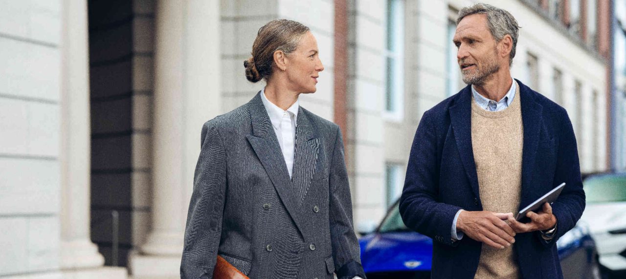 Zwei Personen gehen vor einem Gebaeude mit Saeulen.