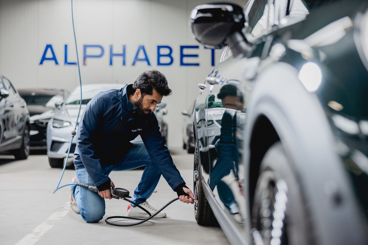 Ein Mann kniet vor einem Autoreifen in einer Werkstatt und benutzt die Luftpumpe um den Reifen zu füllen. 