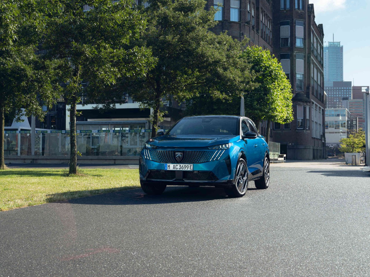 Frontansicht eines blauen Peugeot Autos das in einer urbanen Umgebung mit einem Park steht.