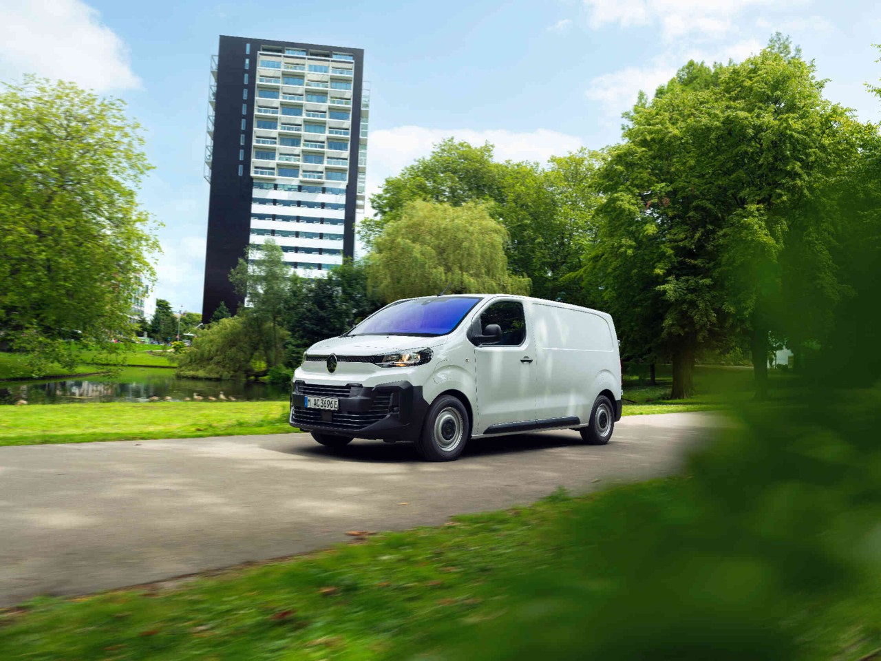 Weisser Lieferwagen faehrt durch gruene Parklandschaft.