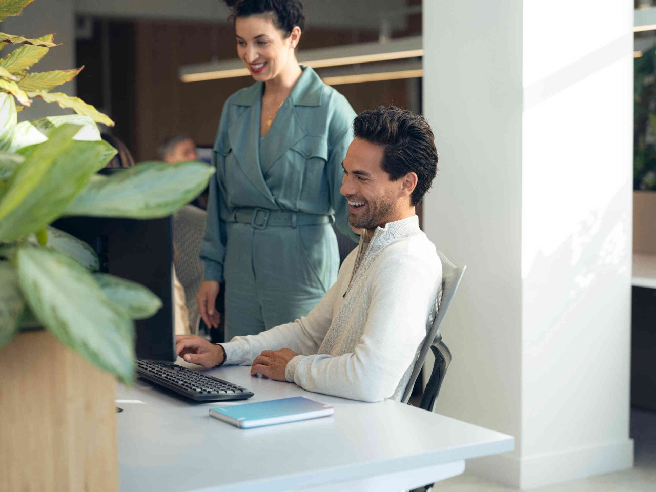 Zwei Personen lachen und blicken auf Computer in hellen Buero.