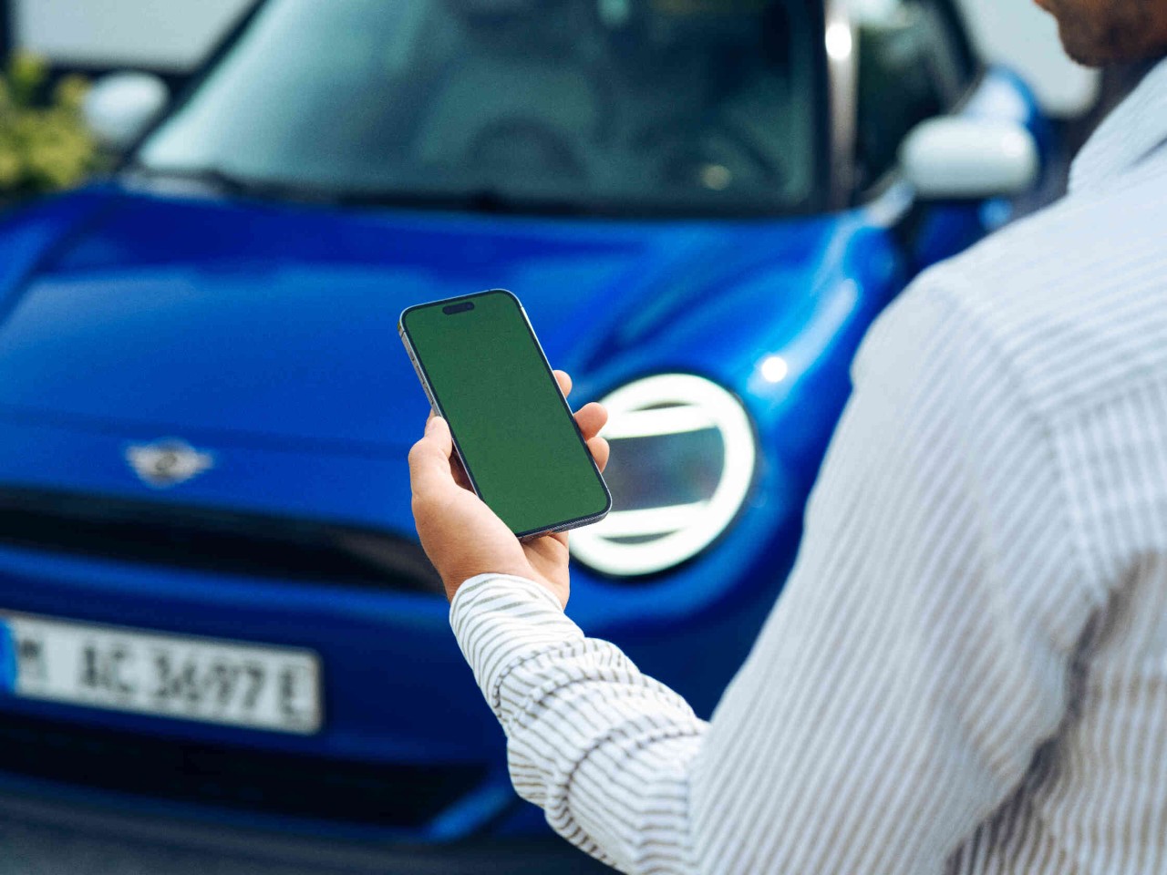 Mann blickt auf Handy und steht vor blauem MINI Auto.