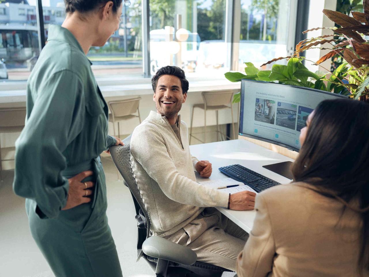 Personen sitzen laechelnd vor grossem Computer Bildschirm.
