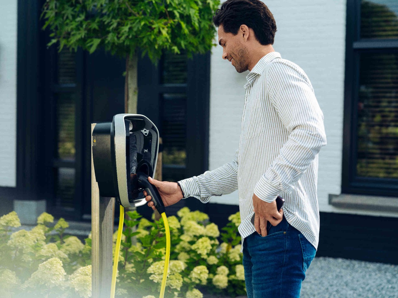 Mann greift Stecker einer E-Ladestation und steckt sein Handy in die Hosentasche.