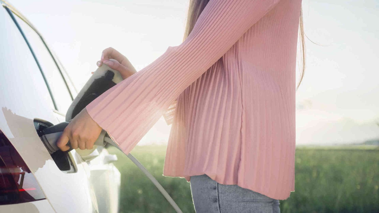 Frau steckt Ladekabel an weisses Elektrofahrzeug