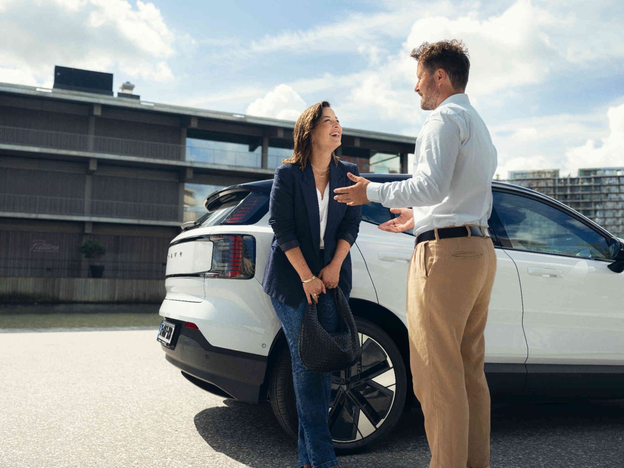 A woman is leaning against a white car and talking to a man.