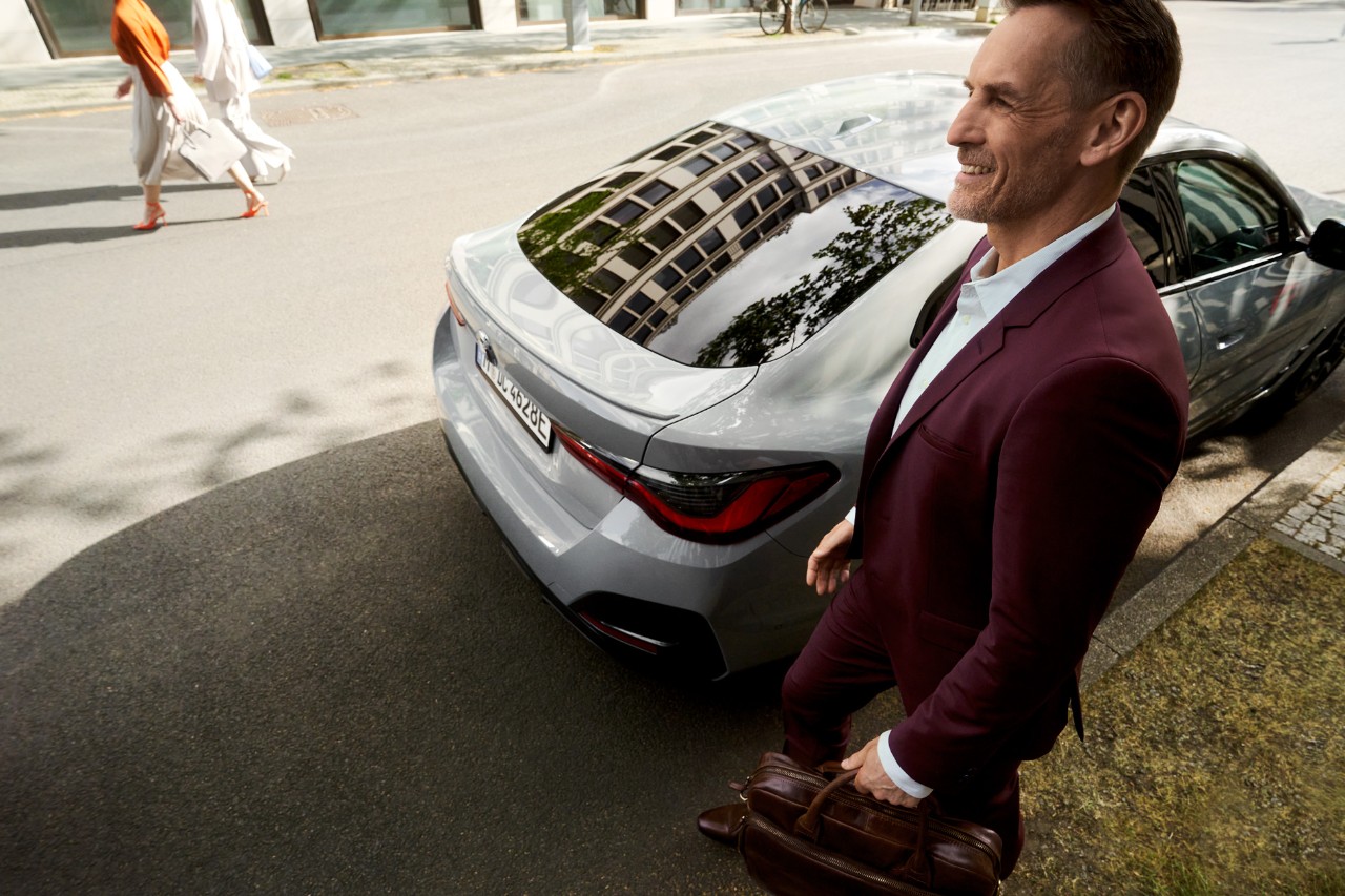 Man in a suit in front of a parked vehicle.