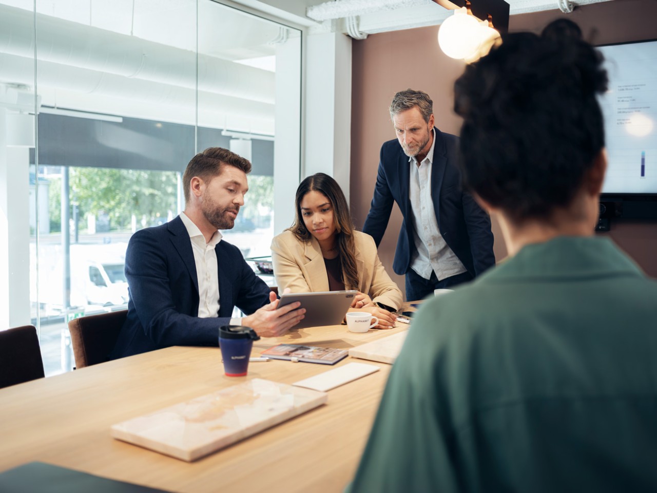 People in an office meeting room looking at a tablet being help by one of the people.