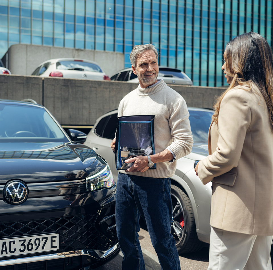 Two people stand next to a Volkswagen.