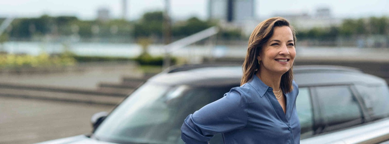 Woman smiling stood in front of a car.