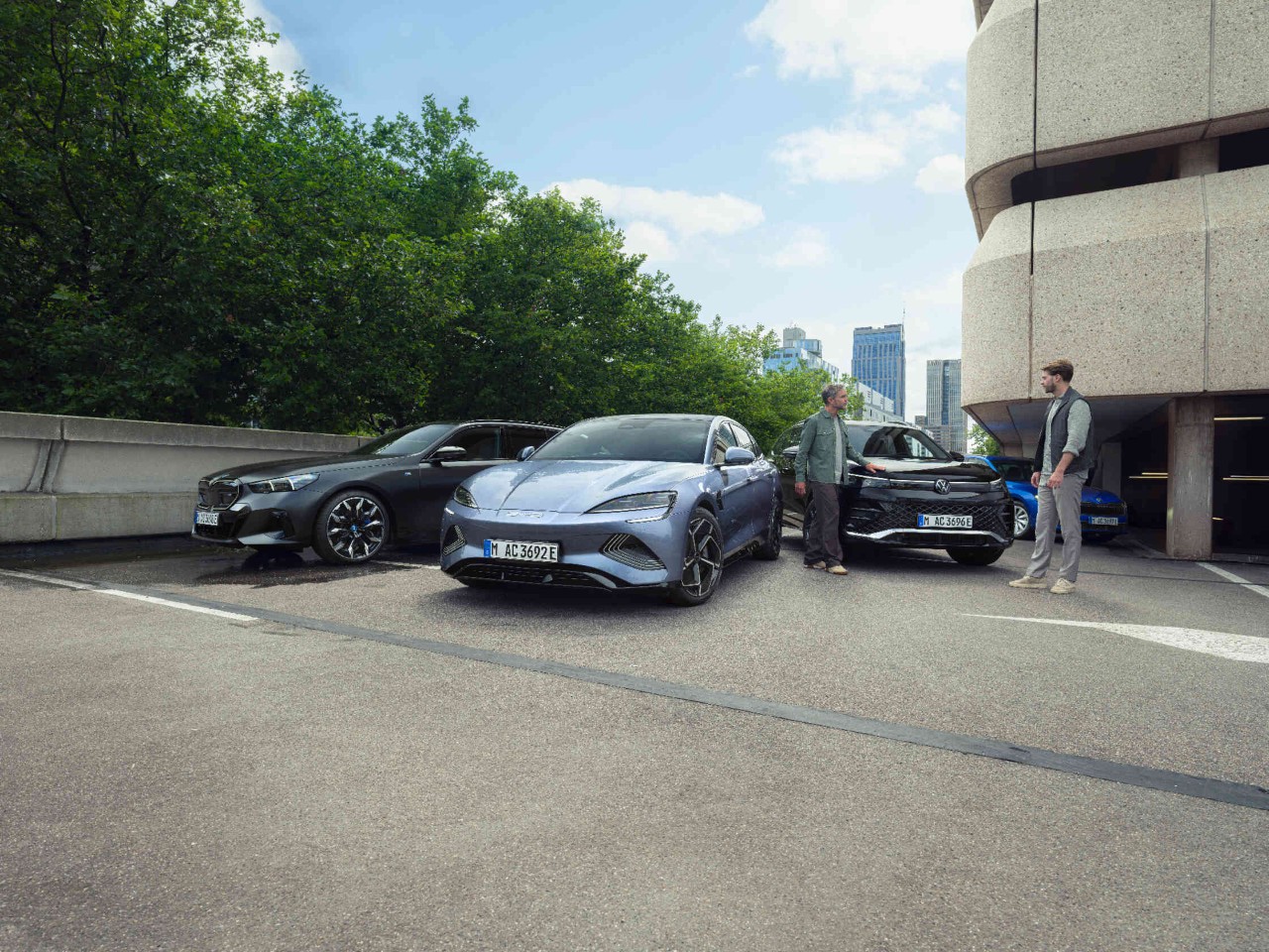 Two men next to three cars in a car park.