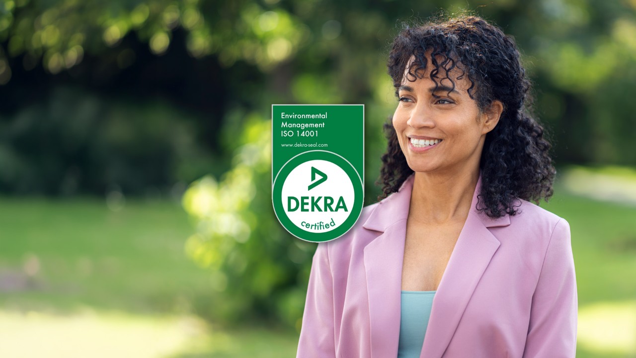 Smiling woman outdoors wearing a pink blazer, beside a DEKRA ISO 14001 certification badge.