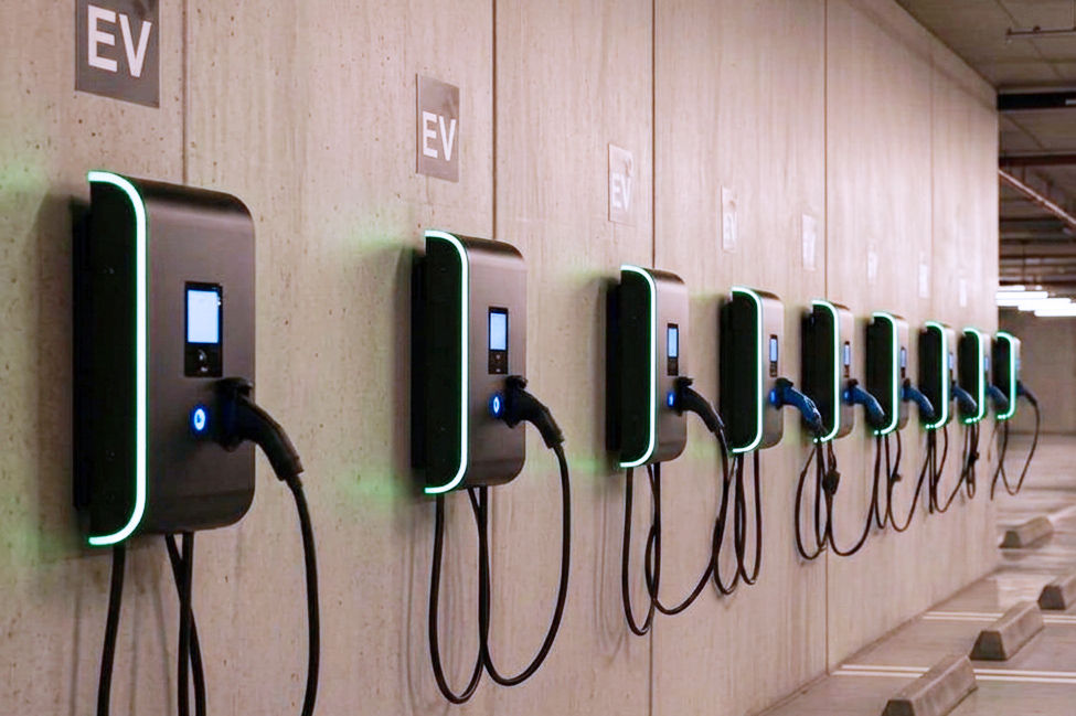 Several electric vehicle charging stations mounted along a wall in an indoor parking area.